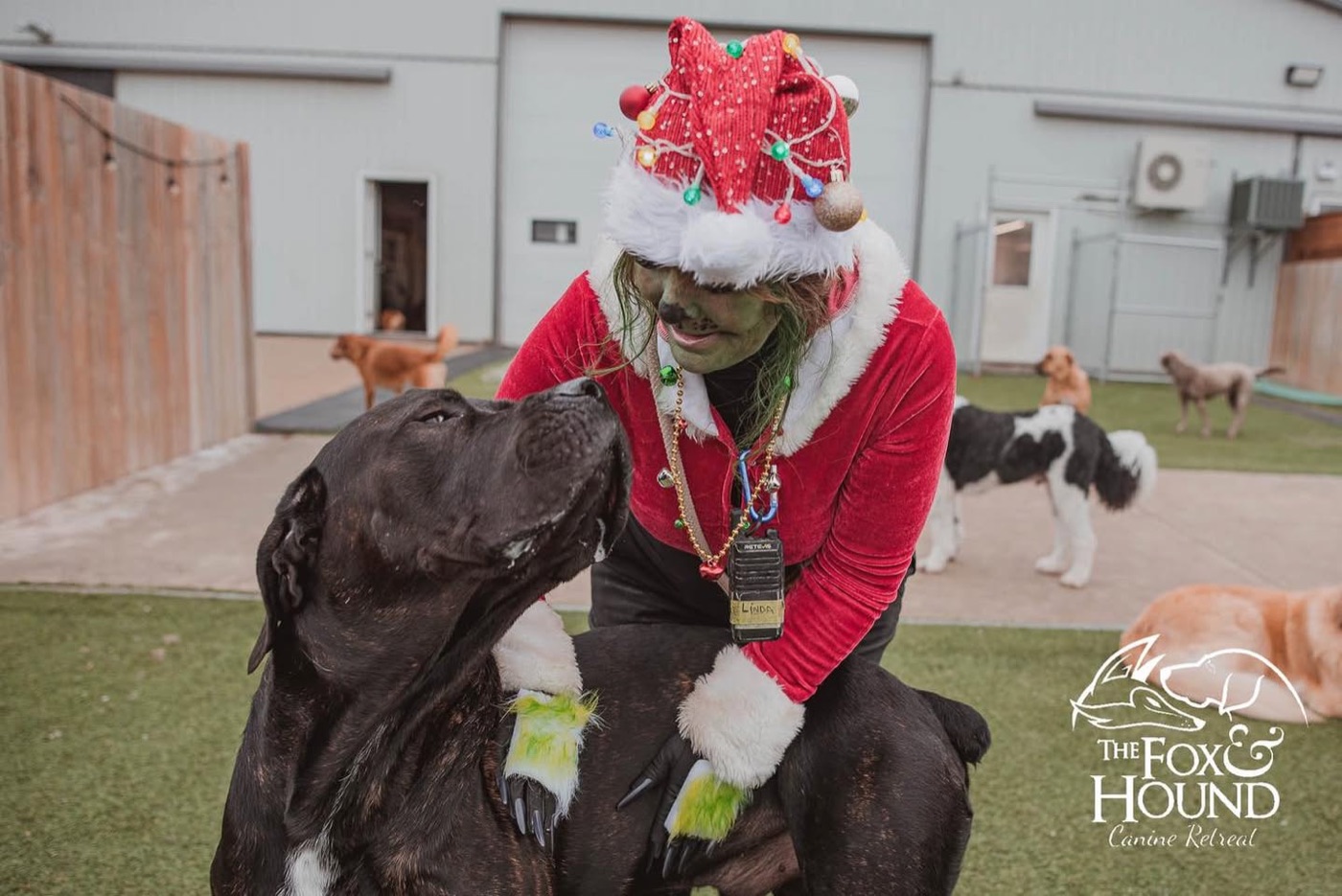 An F&H team member dressed as the Grinch, posing with a black dog